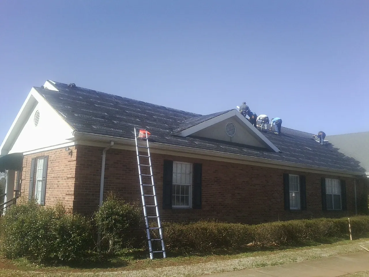 Crew tearing shingles off a brick ranch roof with a ladder set — Emergency Roof Repair work by our crew in Mount Carmel